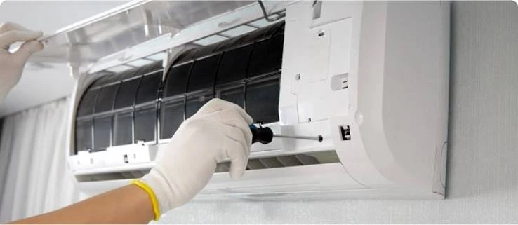 Gloved technician servicing the open front panel of a wall-mounted air conditioner