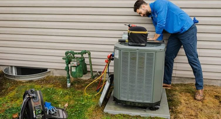 Technician servicing an outdoor air conditioning condenser beside a home